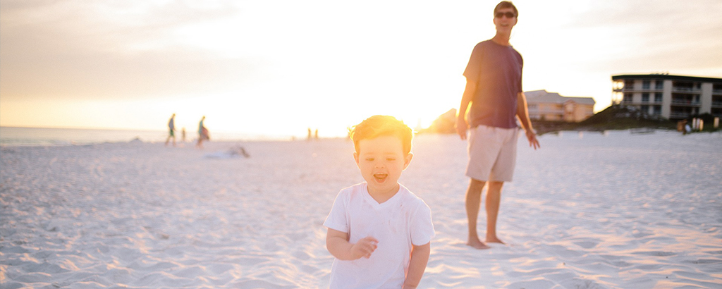joven viendo a su hijo caminar en la playa de cancun